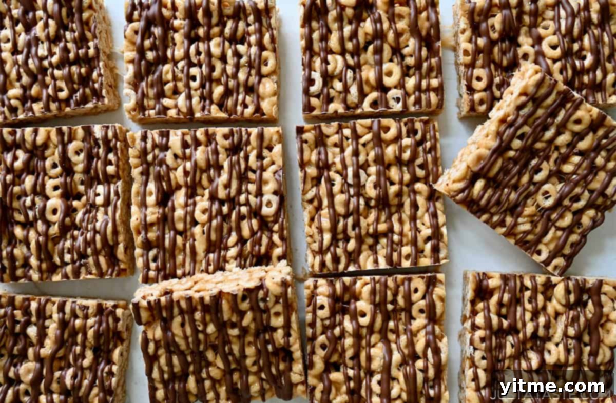 Peanut Butter Cheerios Marshmallow Bars 6 Perfectly cut squares of peanut butter Cheerios bars, elegantly drizzled with chocolate, arranged invitingly on a cutting board, showcasing their irresistible appeal.