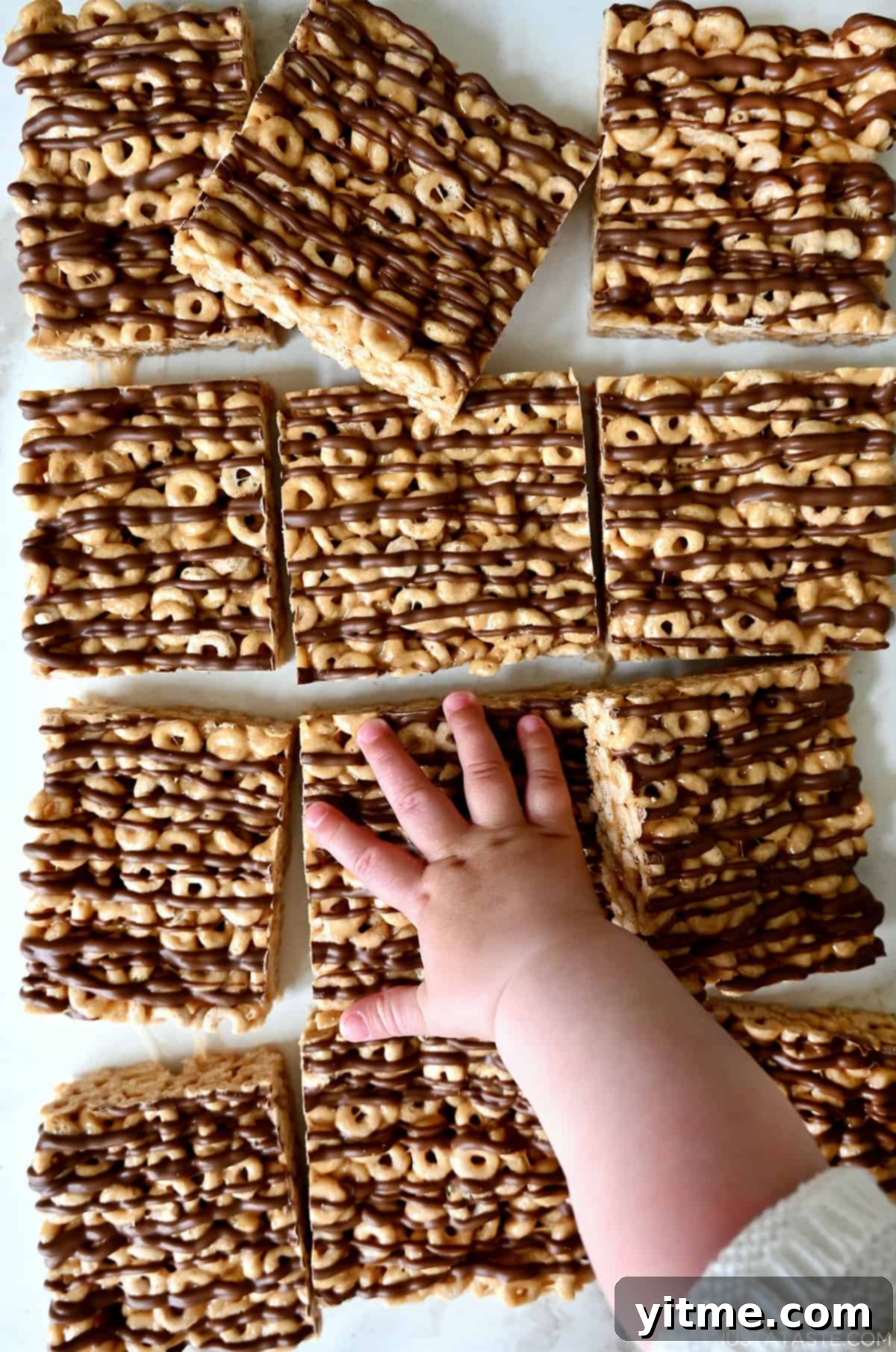 Peanut Butter Cheerios Marshmallow Bars 7 A child's hand reaches for a peanut butter Cheerio's marshmallow treat, highlighting its deliciousness and kid-friendly appeal.