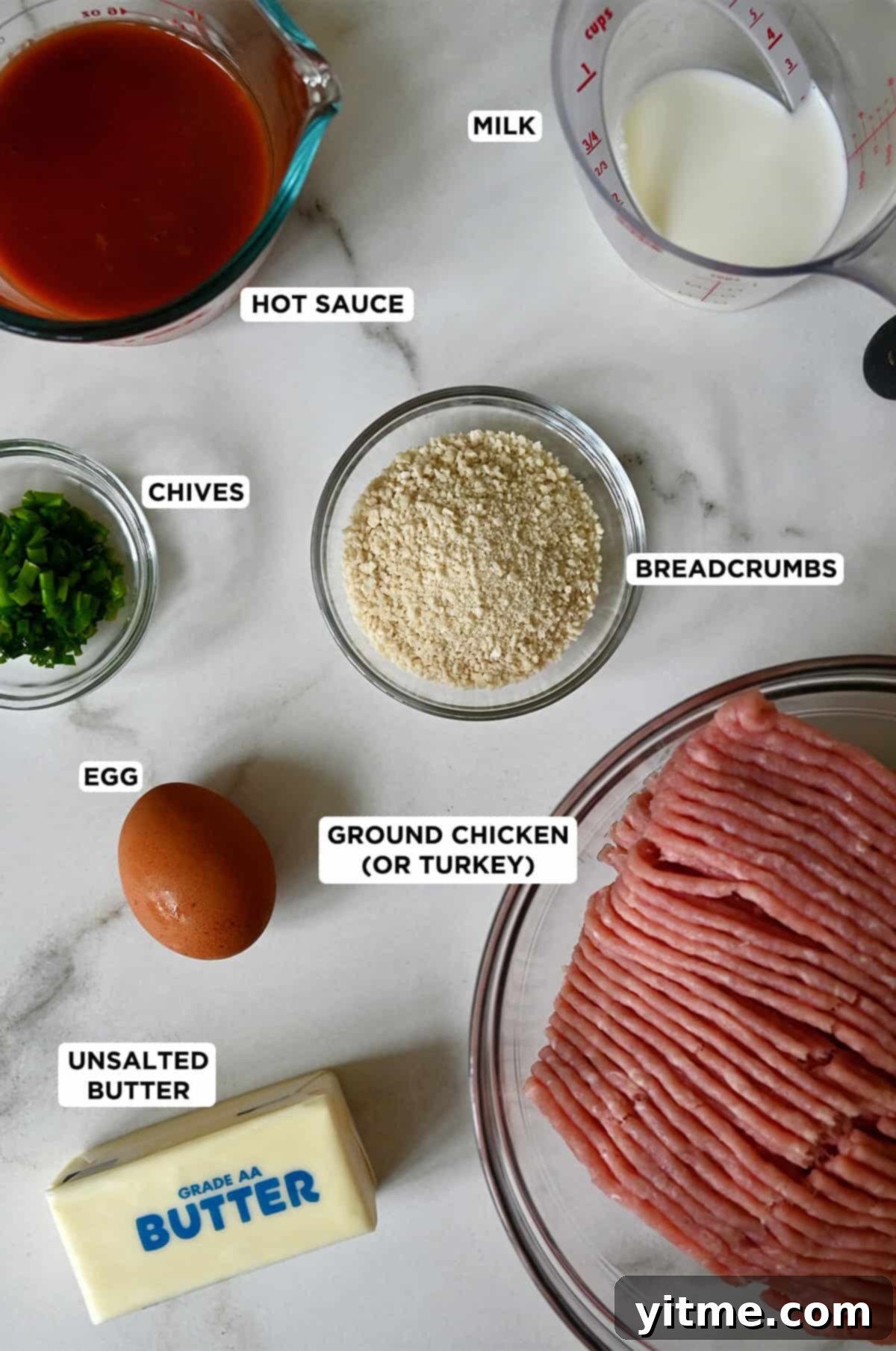 Buffalo chicken meatball ingredients in glass bowls, including ground chicken, butter, an egg, chopped chives, Panko breadcrumbs, hot sauce and milk.