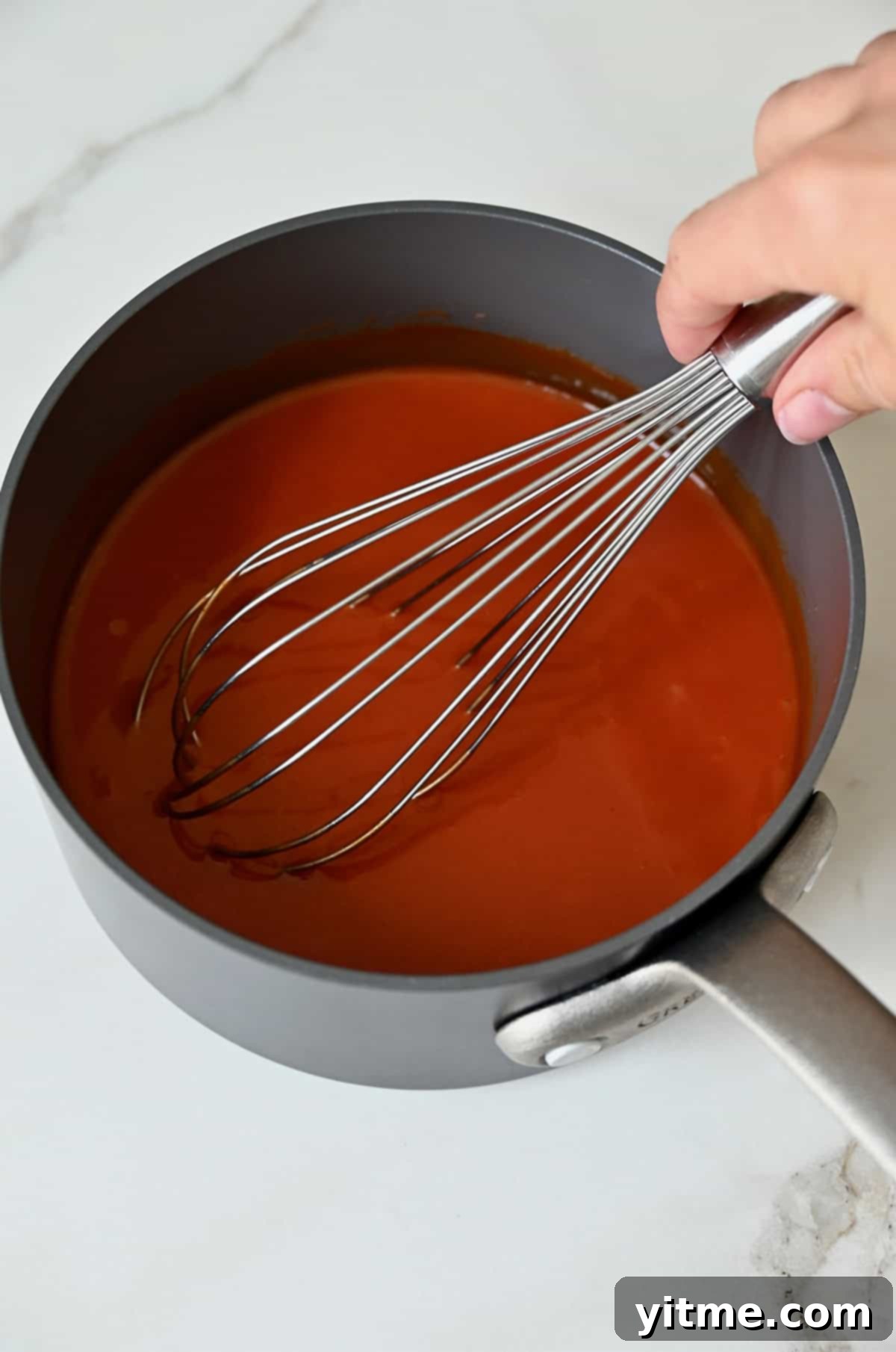Homemade buffalo sauce in a saucepan being whisked by hand.