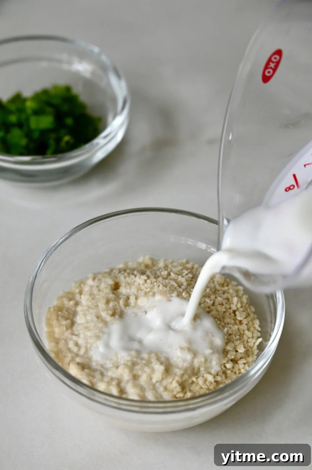 Milk being poured over Panko breadcrumbs in a glass bowl.