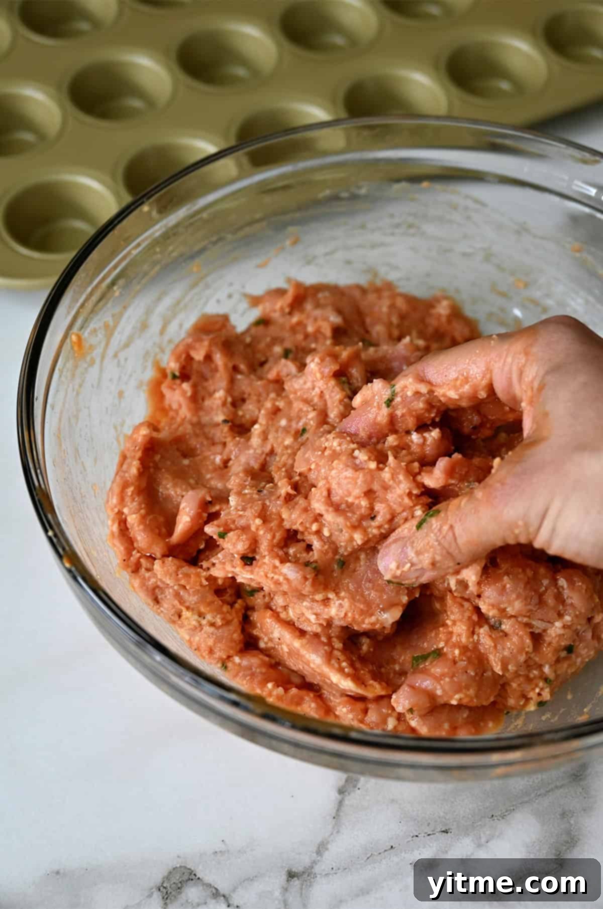 A hand grabbing meatball mix from a bowl to shape into a ball.