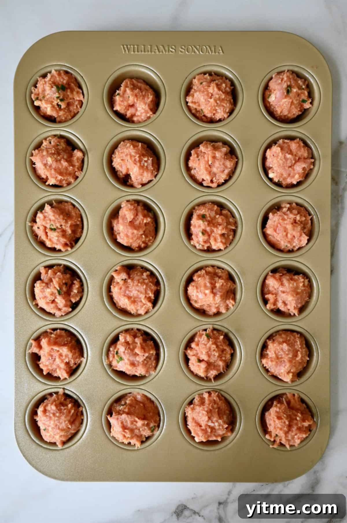 Unbaked chicken meatballs in a mini muffin pan.