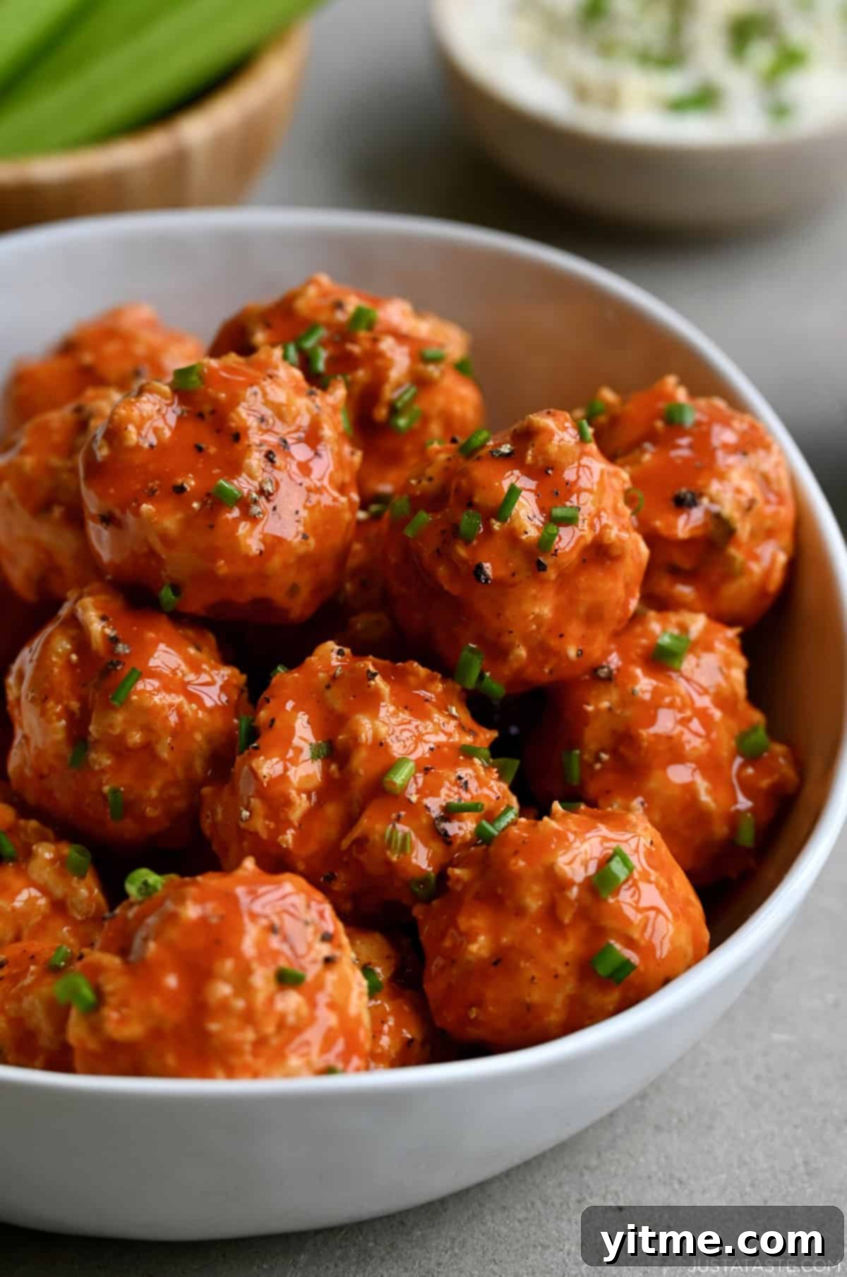 Mini buffalo chicken meatballs with chives in a large white bowl.