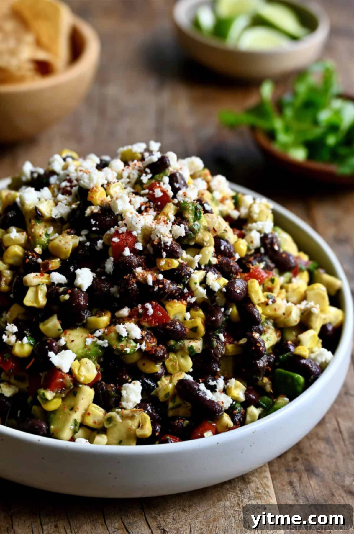 A white serving bowl containing black bean and corn salad with avocado and cojita cheese all tossed in a tangy lime vinaigrette.