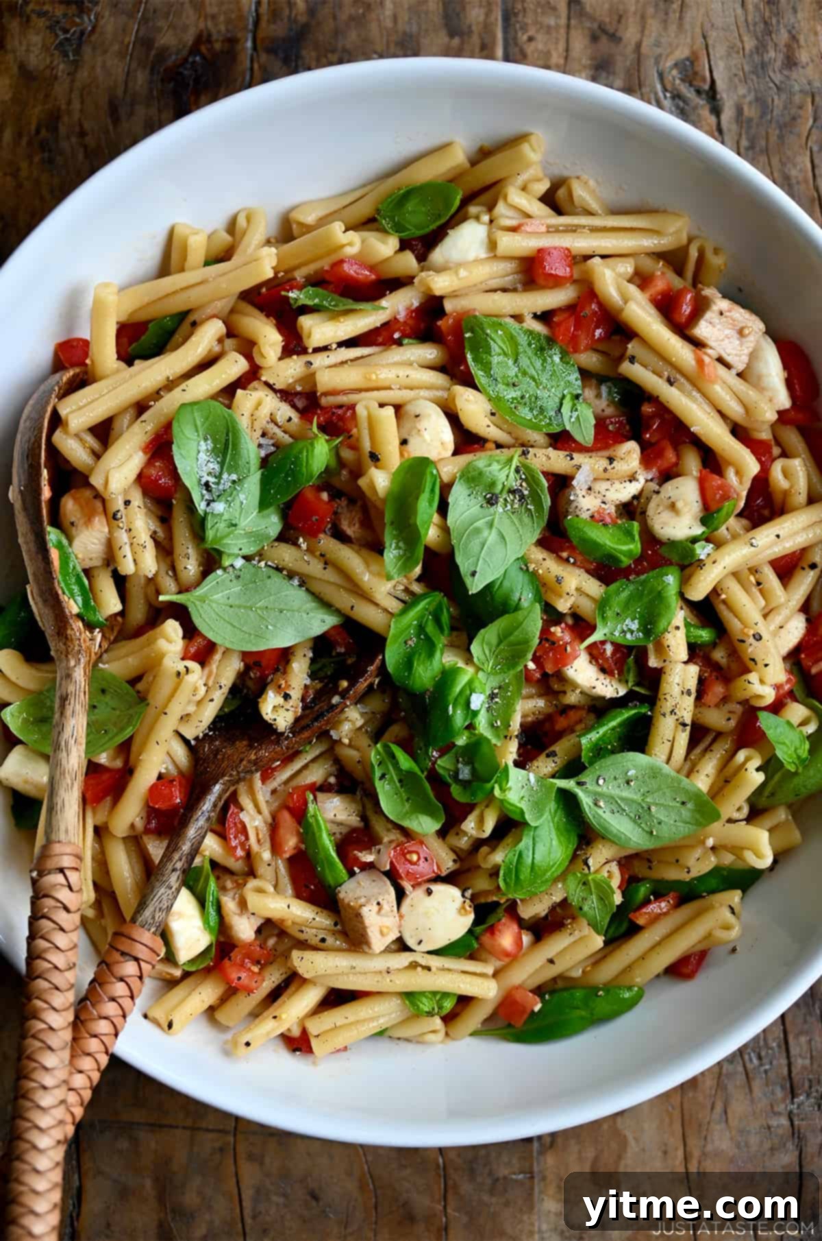 A top-down view of a large serving bowl containing Caprese pasta salad garnished with fresh basil leaves.