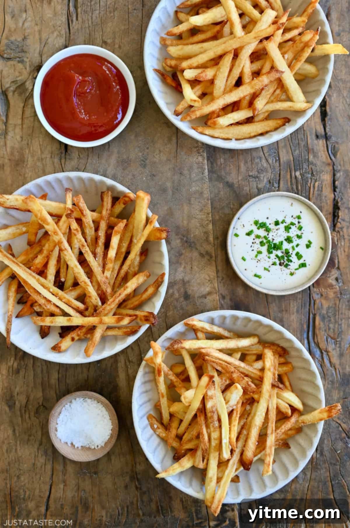 French fries three ways: deep fried, air fried and baked. Three smalls bowls containing ketchup, ranch dressing and sea salt are nearby.