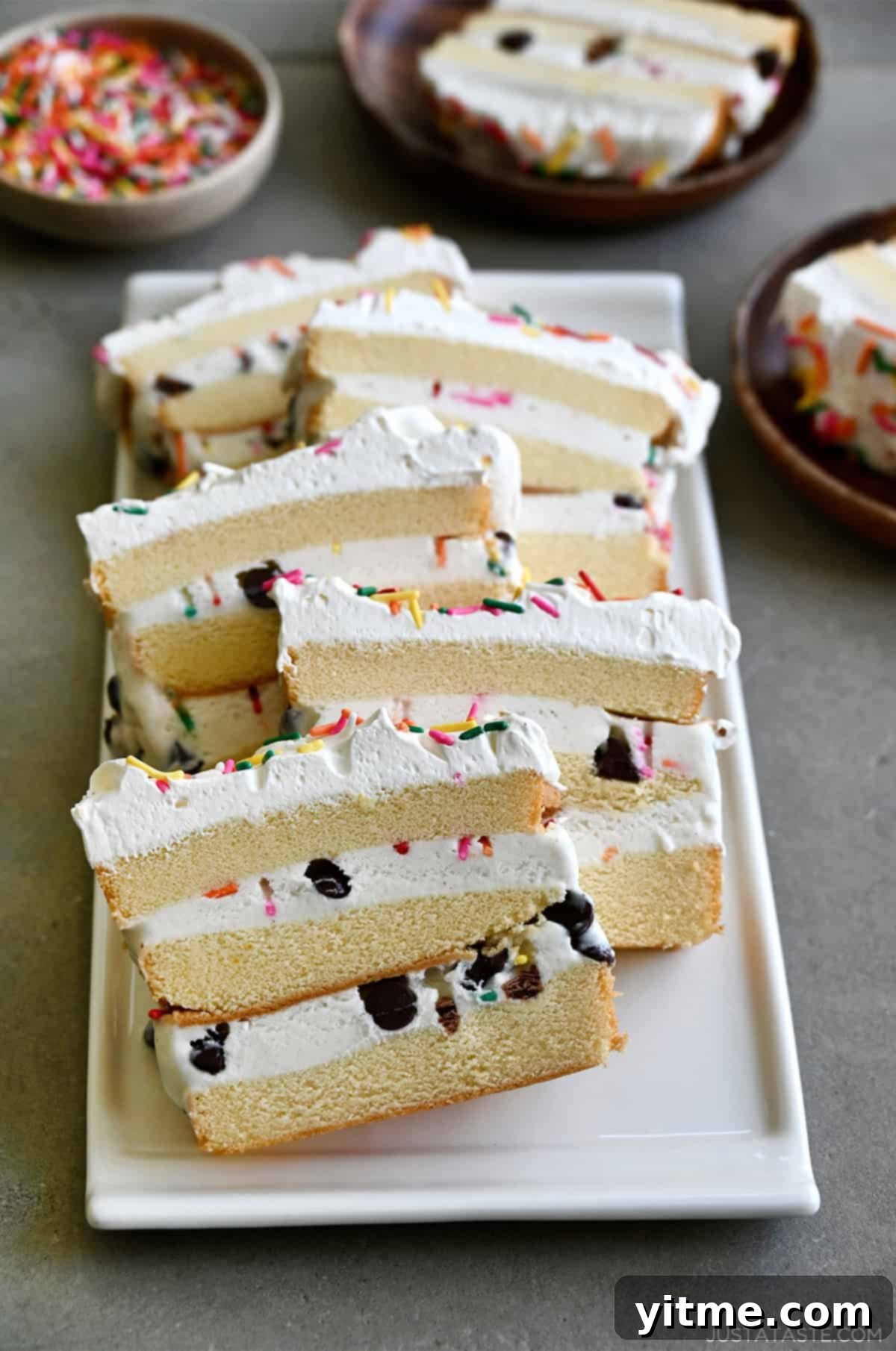 Slices of layered ice cream cake made with store-bought pound cake, ice cream, chocolate chips and sprinkles topped with whipped cream.
