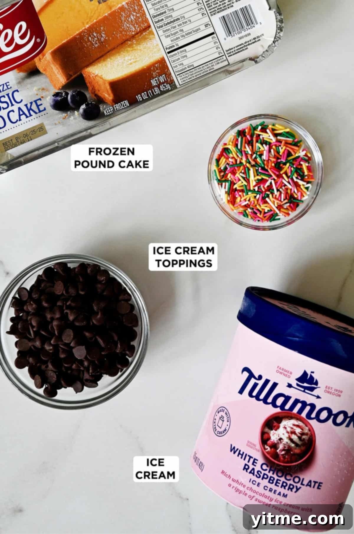 A small tub of Tillamook White Chocolate Raspberry ice cream next to a Sara Lee pound cake and two small bowls containing chocolate chips and sprinkles.