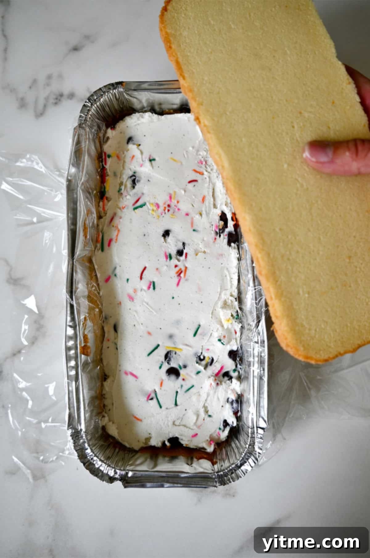 Ice cream in an even layer with a slice of pound cake being placed on top.