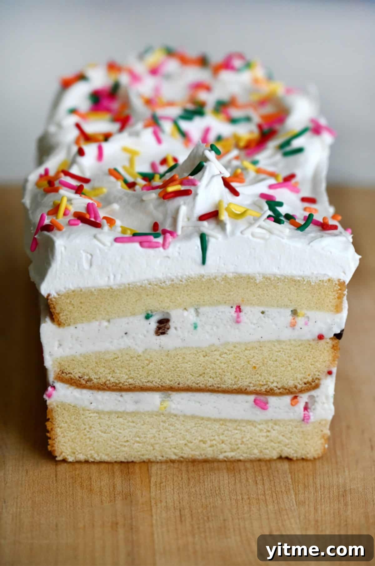 Layered ice cream pound cake topped with whipped cream and rainbow sprinkles.
