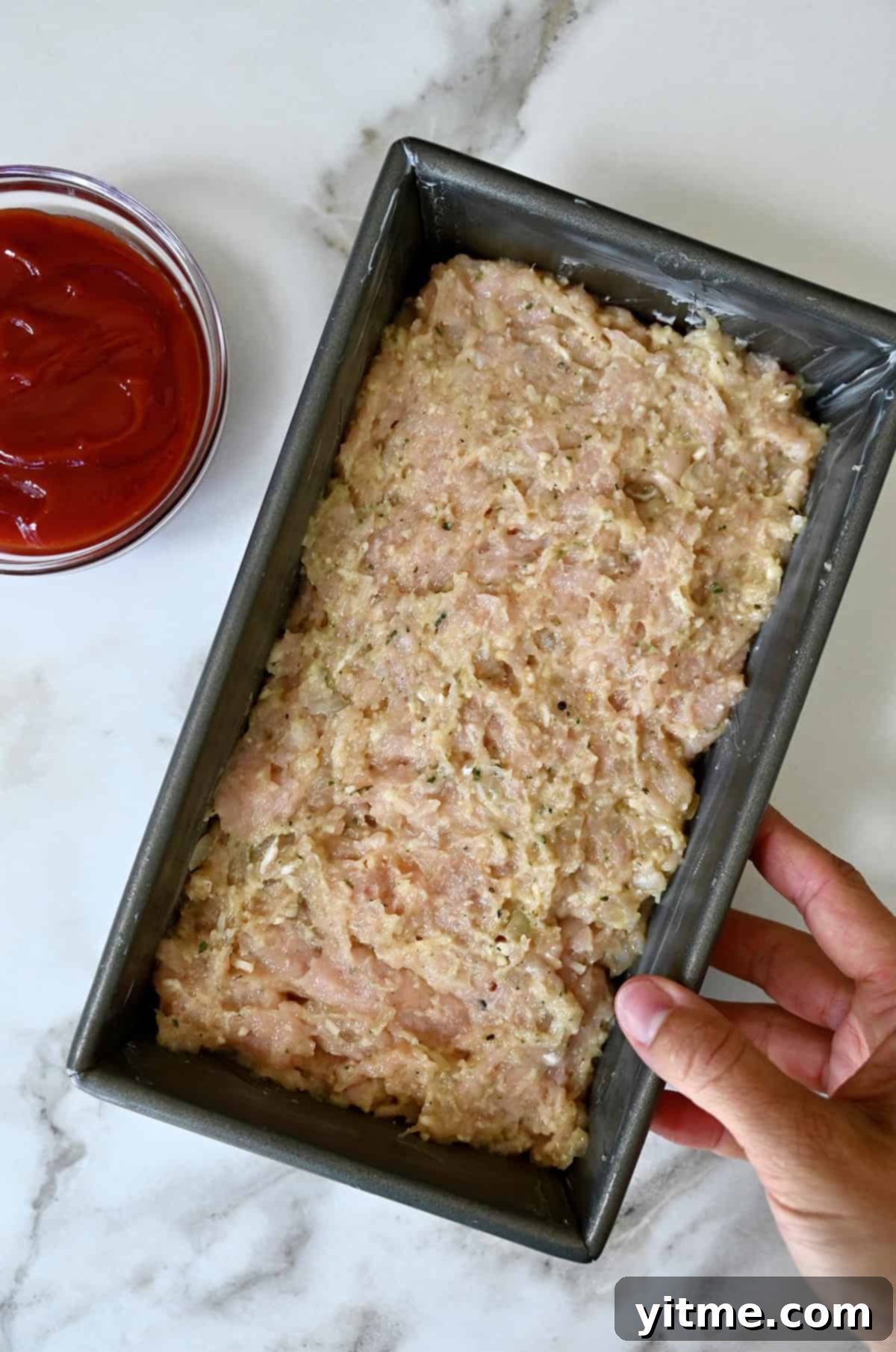 Raw, uncooked ground chicken meatloaf mixture pressed evenly into a greased loaf pan, ready for baking.