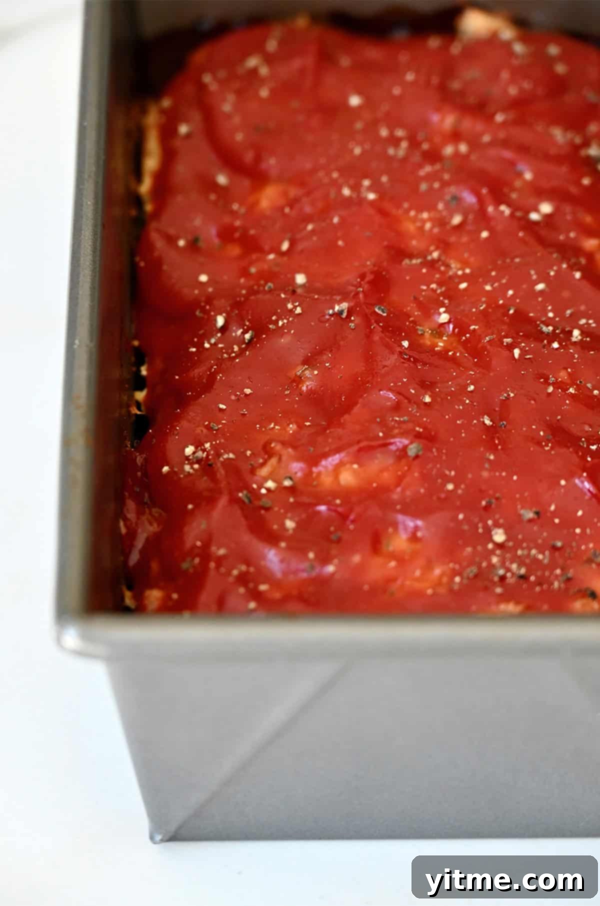 A golden-brown, perfectly glazed chicken meatloaf, still warm in its loaf pan, glistening with its tangy ketchup topping.
