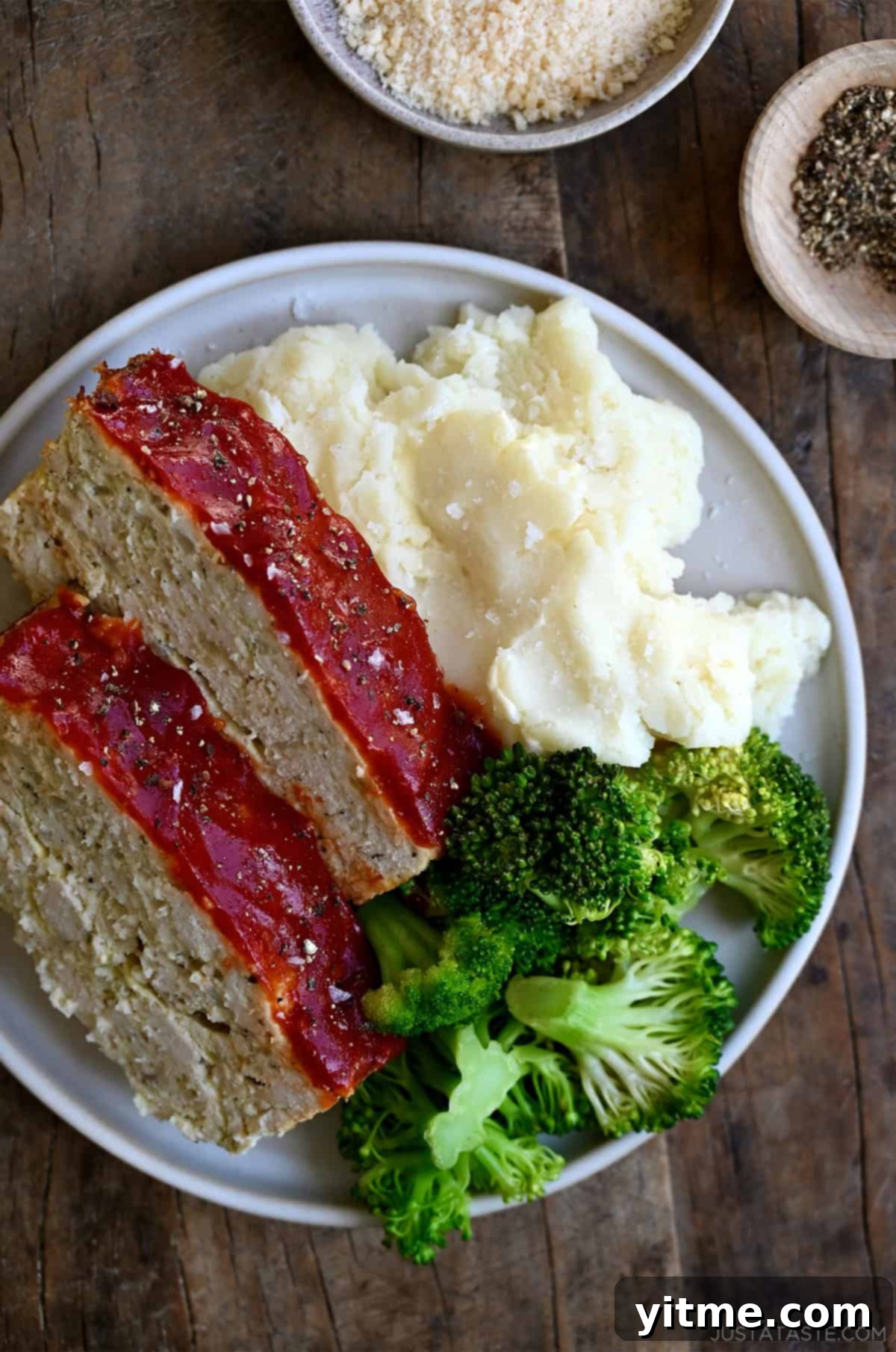 Two slices of classic chicken meatloaf on a dinner plate with steamed broccoli and mashed potatoes, highlighting the caramelized glaze and tender texture.