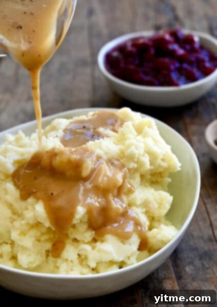 Homemade gravy being poured over mashed potatoes.