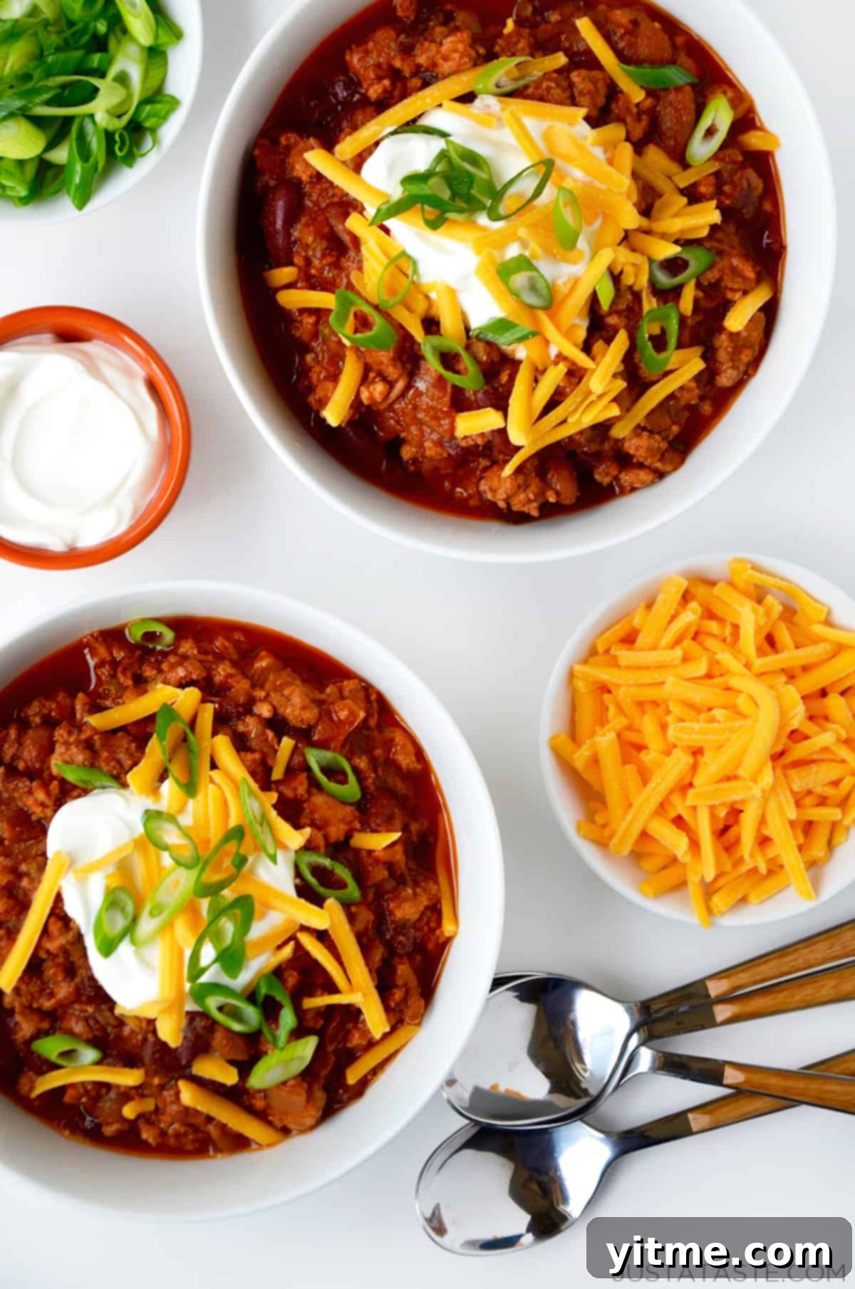 Bowls of ground chicken chili topped with sour cream, cheese, and scallions