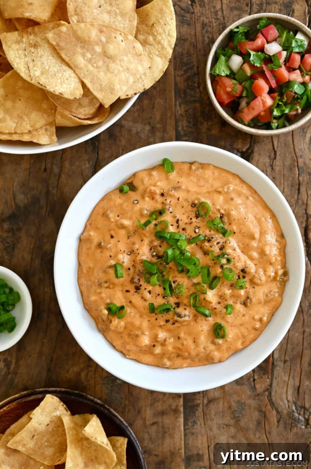 Chorizo queso dip in a white bowl next to a bowl filled with tortilla chips and a small bowl containing pico de gallo.