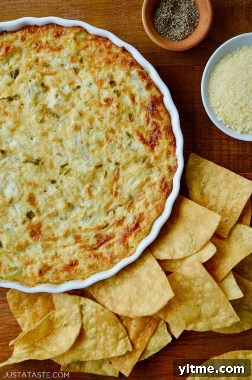 Hot and Creamy Artichoke Dip in a white baking dish surrounded by tortilla chips.