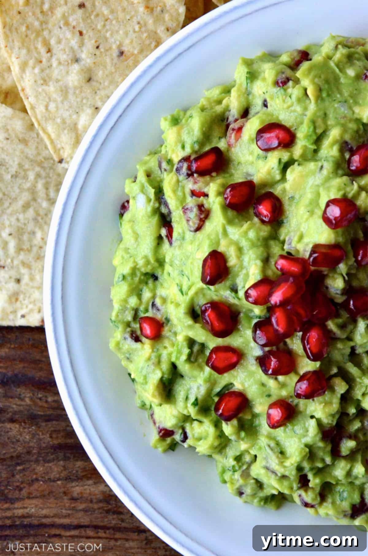 A bowl of pomegranate guacamole topped with extra pomegranate seeds. Tortilla chips are beside the bowl.
