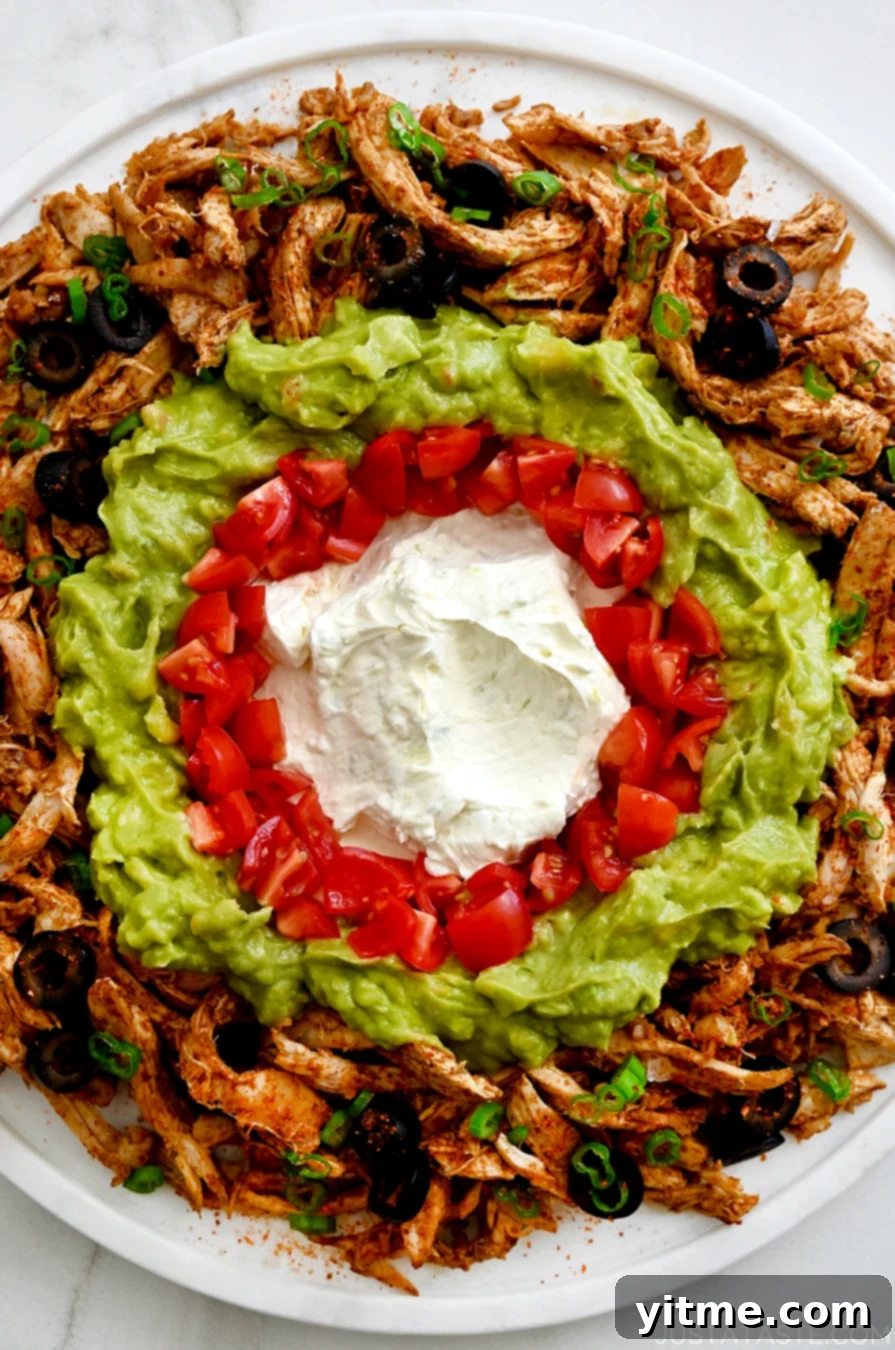 A close-up view of chicken taco dip featuring cream cheese, tomatoes, guacamole and black olives