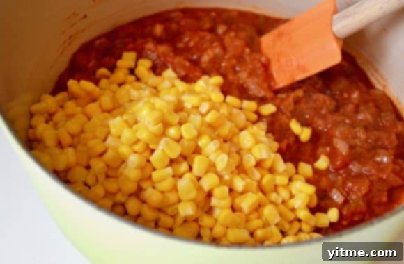 A stock pot containing Salsa Corn Chowder with a pile of yellow corn