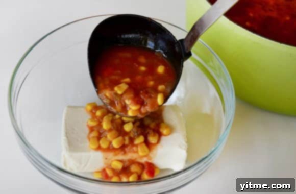 A clear bowl containing cream cheese with chowder being ladled in