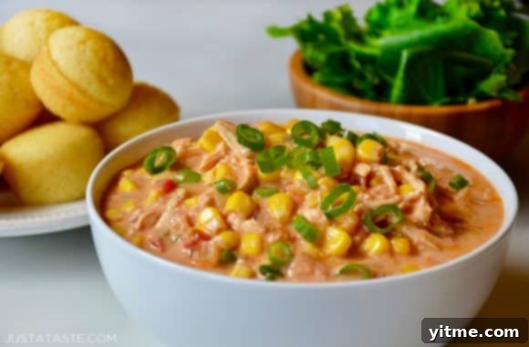 A white bowl containing Salsa Corn Chowder with a salad and corn muffins in the background