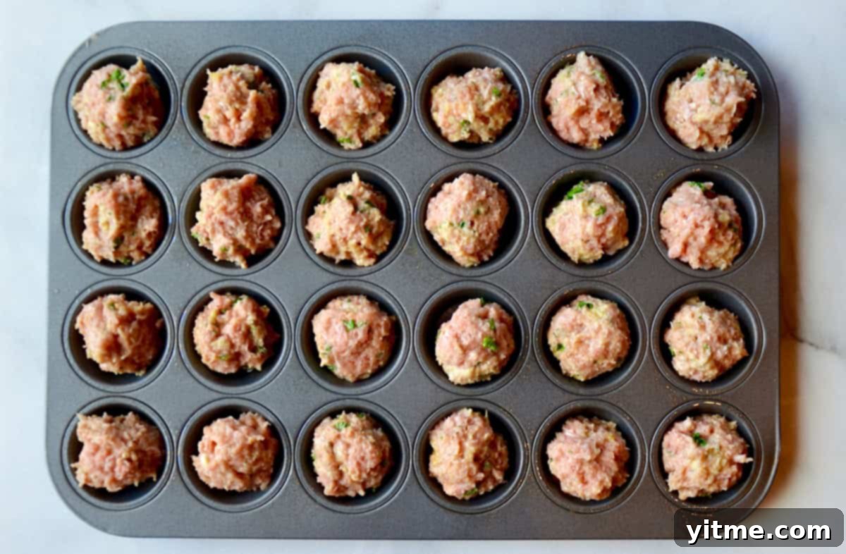 A mini muffin tin holds a raw turkey meatball in each cup.