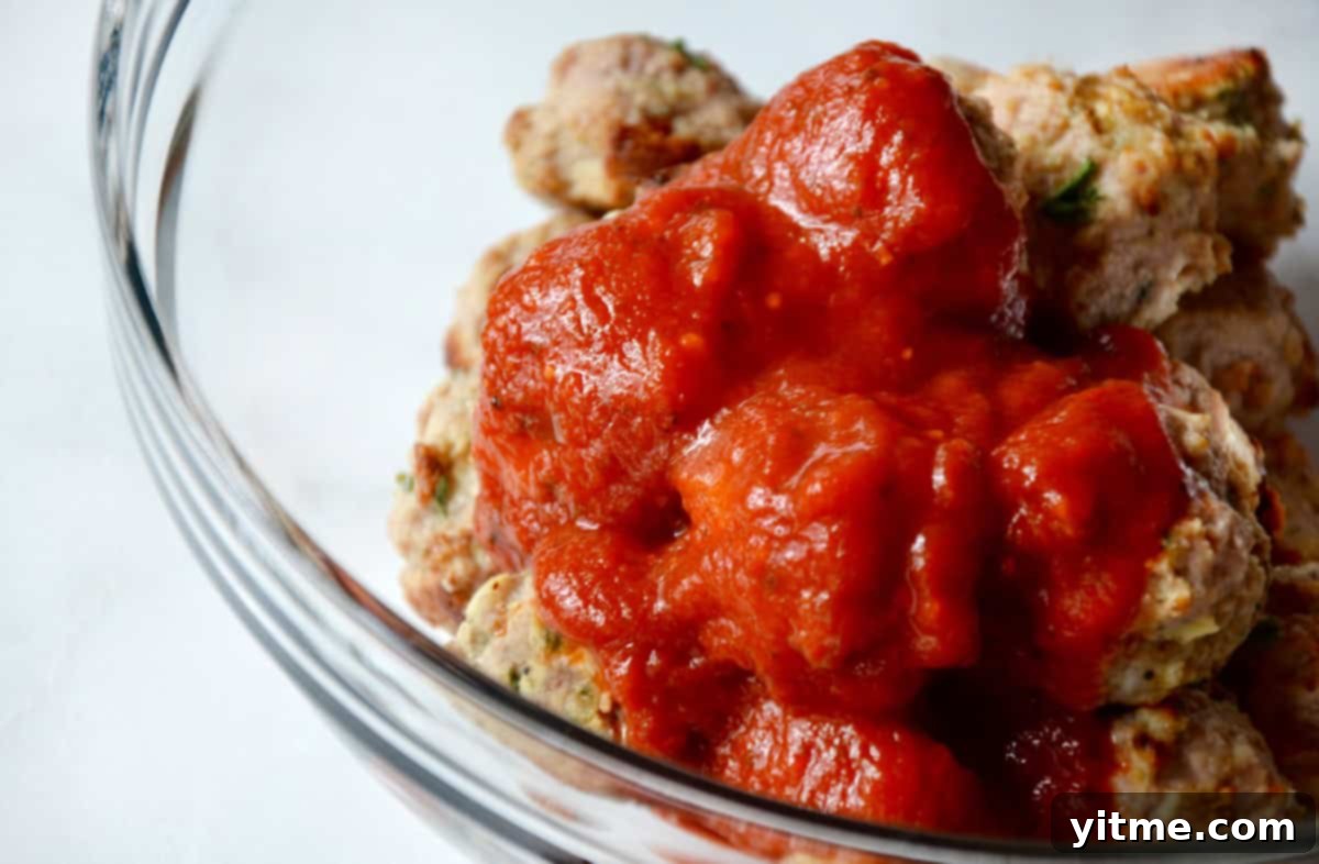 A clear glass bowl holds baked turkey meatballs with tomato sauce poured over them.