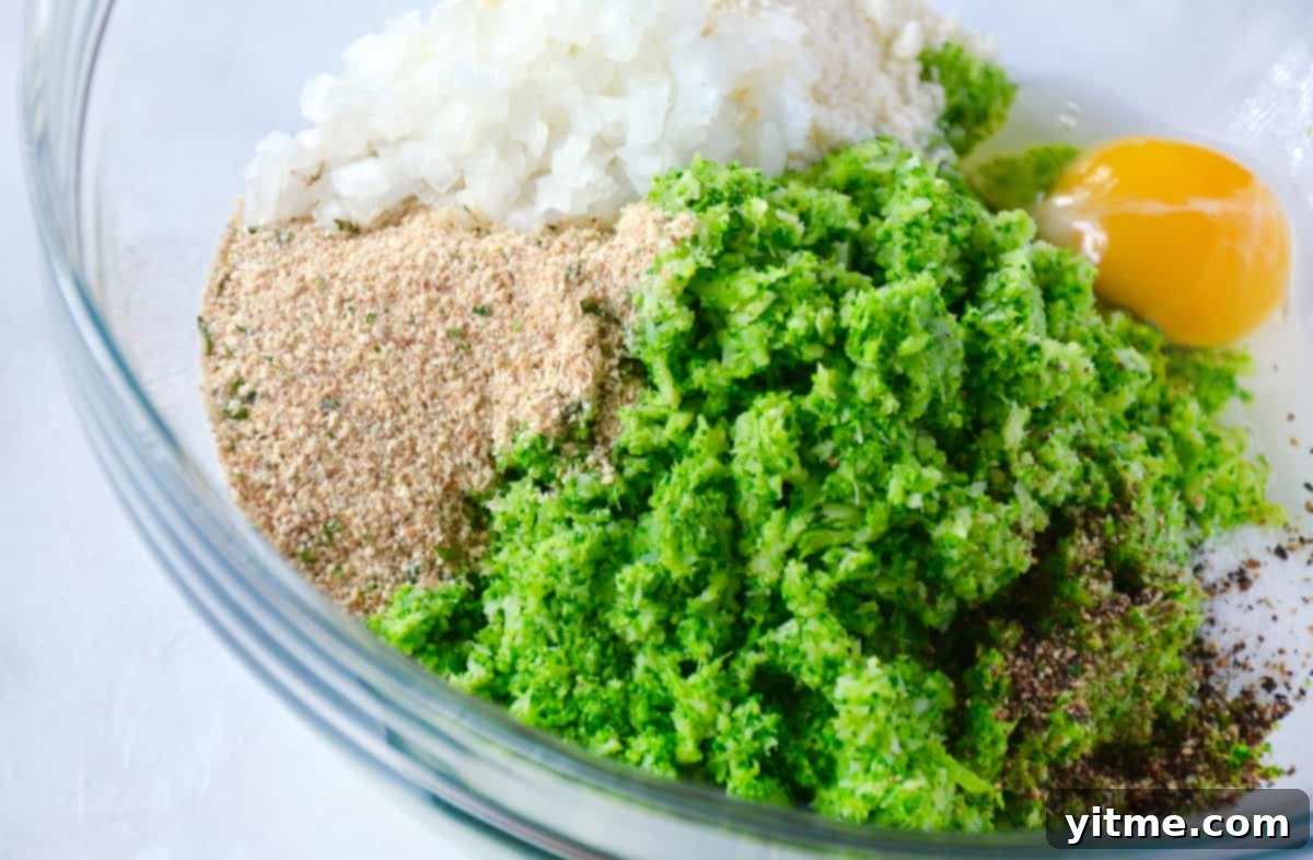 Crispy Baked Broccoli Bites 4 A large glass mixing bowl filled with finely chopped broccoli, along with diced onion, breadcrumbs, grated cheese, and an egg, ready to be mixed into a uniform tot mixture.