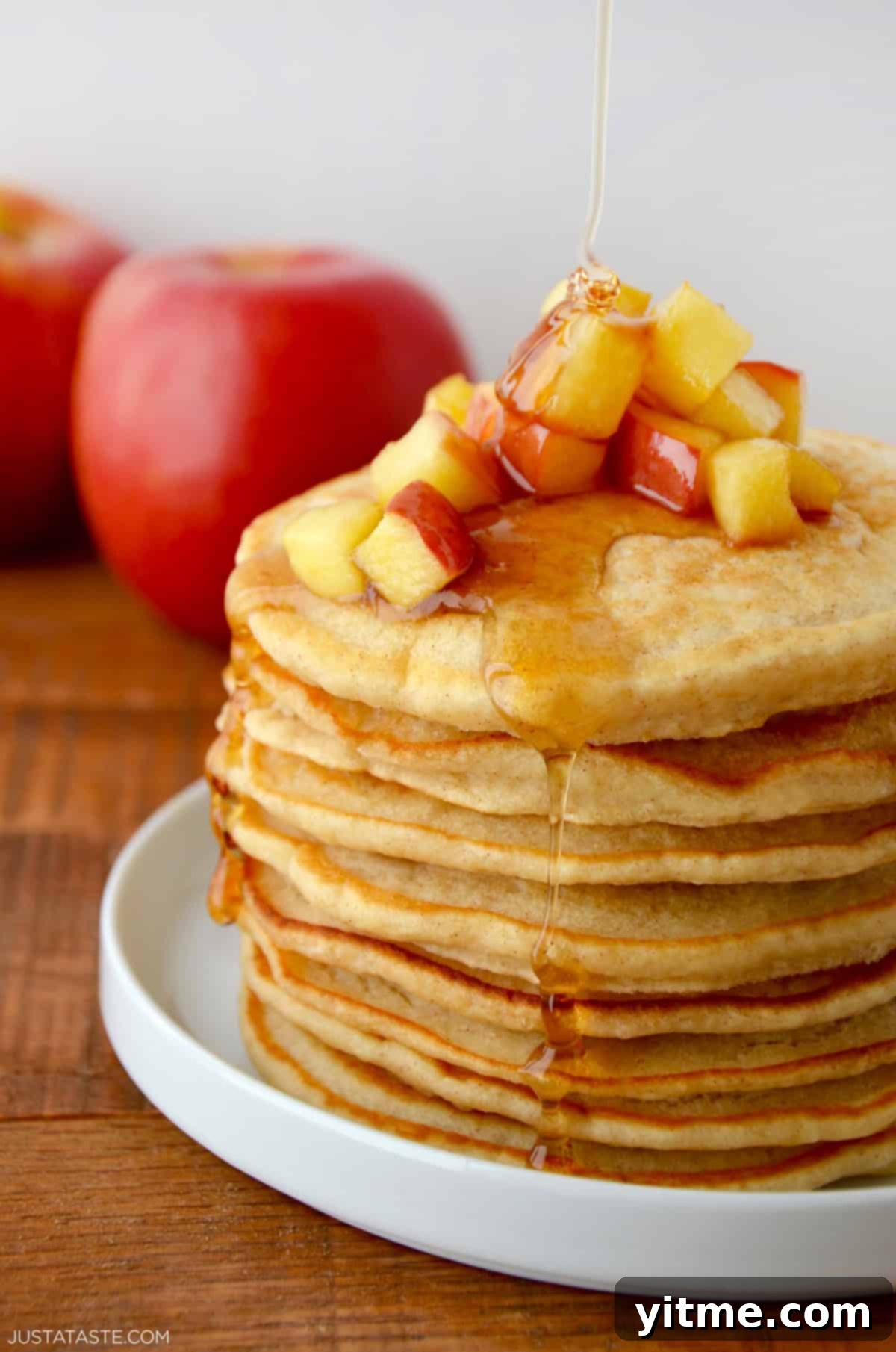A tall stack of fluffy apple pancakes topped with sautéed apples and warm maple syrup.