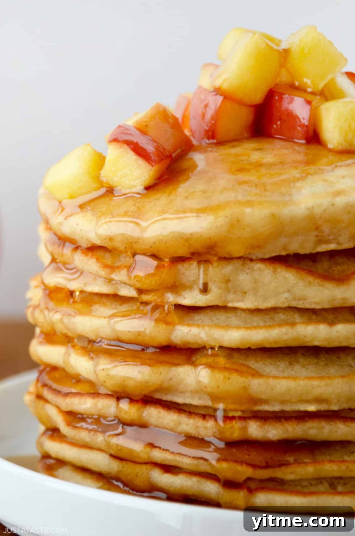 A tall stack of fluffy apple pancakes topped with caramelized sautéed apples and a drizzle of warm maple syrup.