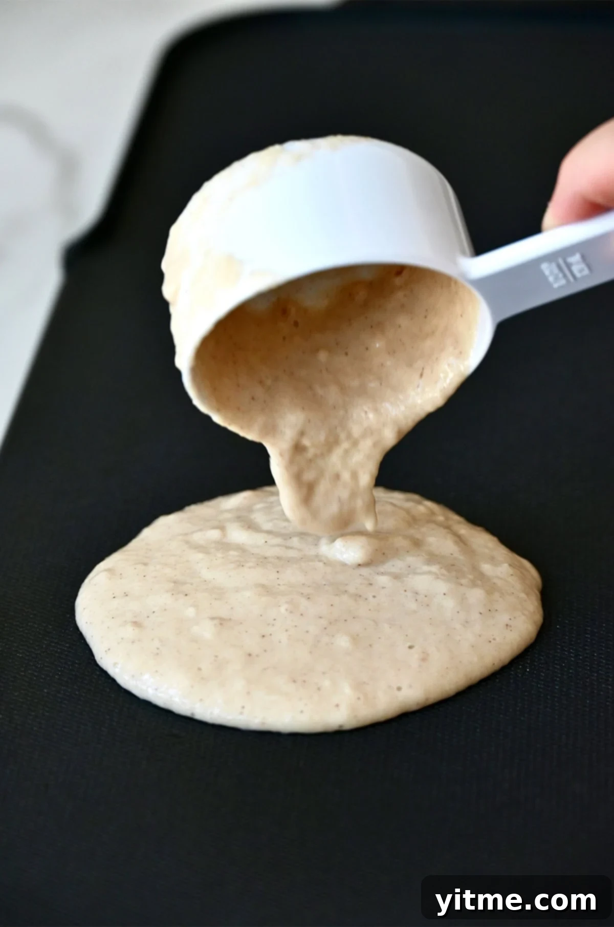 Pouring cinnamon applesauce pancake batter from a measuring cup onto a griddle.
