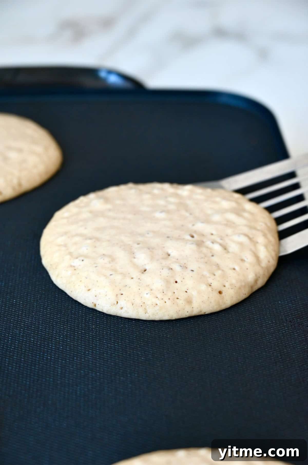 Bubbles forming on the surface of an apple pancake that's cooking on a hot griddle.