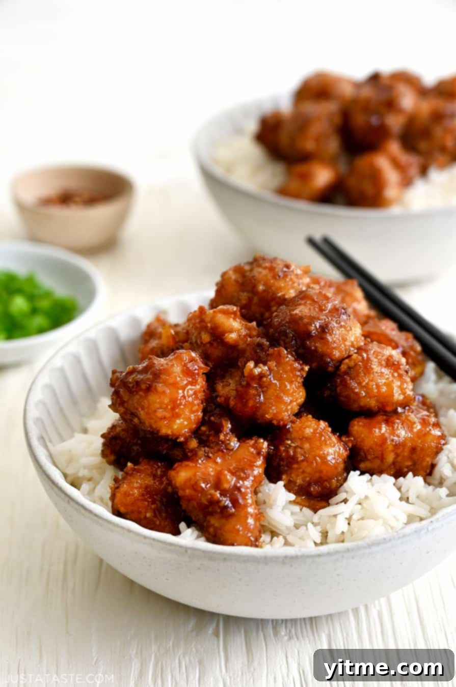 Baked Orange Chicken atop white rice in a bowl with chopsticks