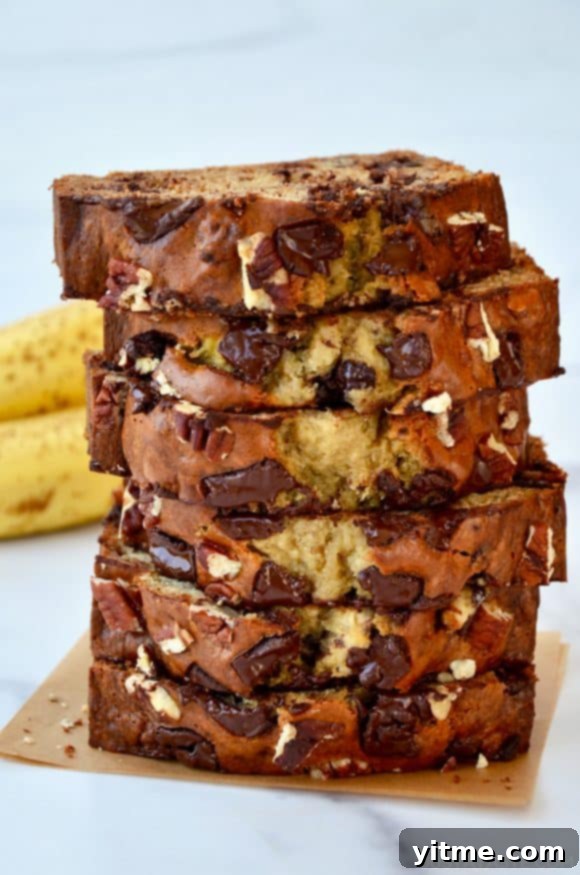 Greek Yogurt Banana Bread Bliss 7 Slices of banana bread stacked on top of each other with bananas in the background.