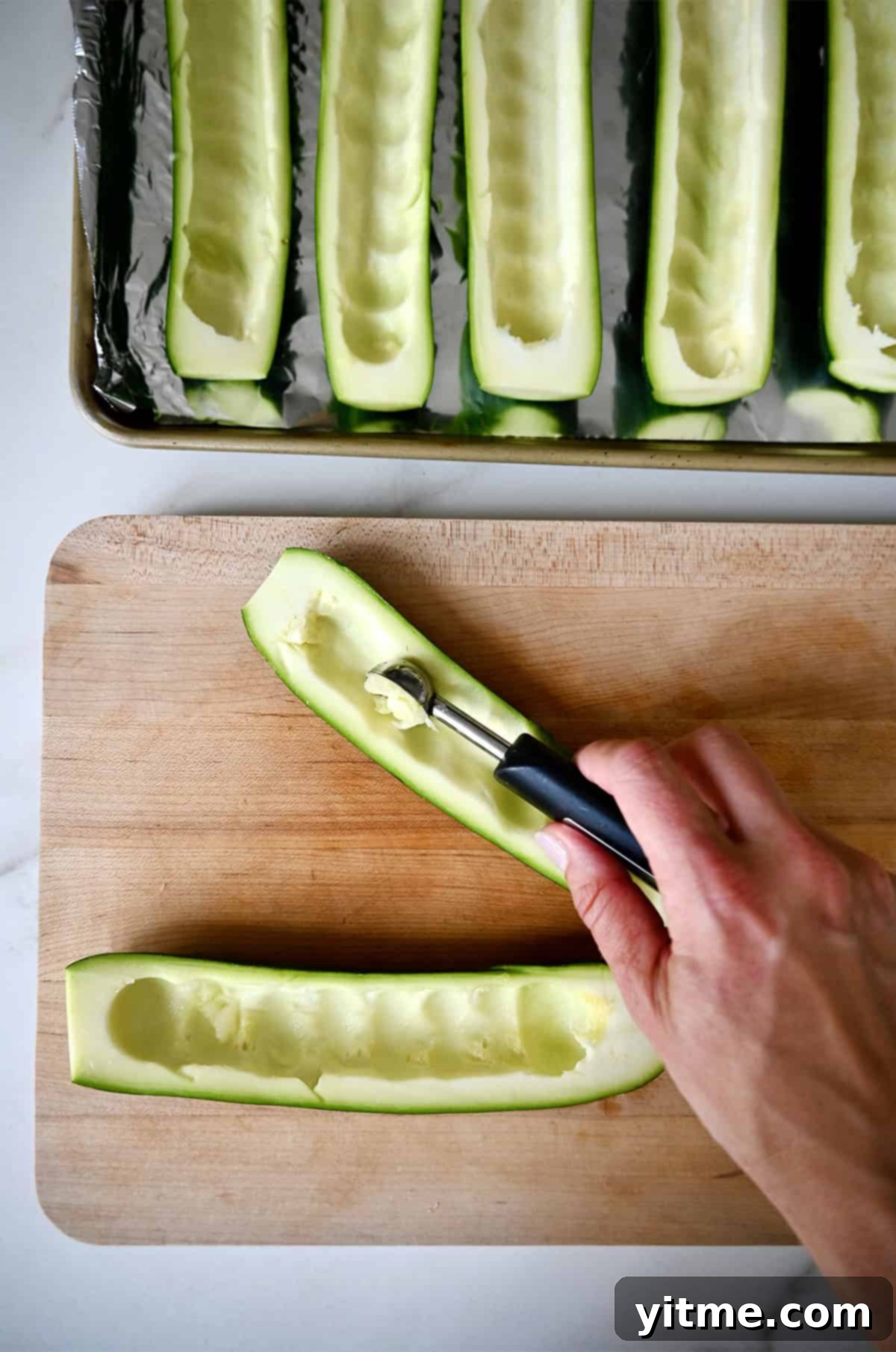 Deliciously Healthy Stuffed Zucchini Boats 4 Scooping out the centers of zucchini with a melon baller.