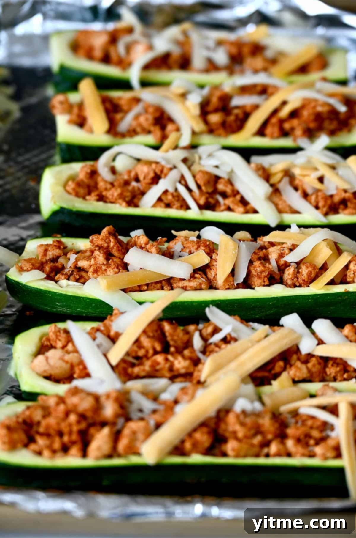 Deliciously Healthy Stuffed Zucchini Boats 7 Stuffed zucchini boats topped with shredded cheese on a foil-lined baking sheet before melting the cheese.