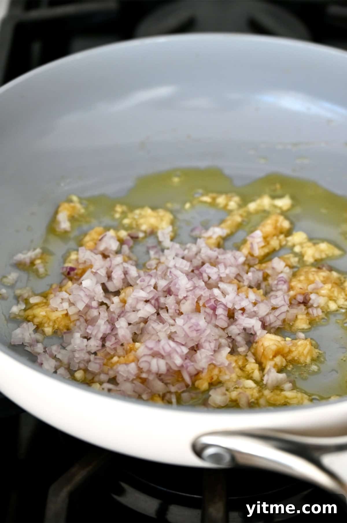 Shallots, garlic, and ginger being sauteed in a pan with oil.