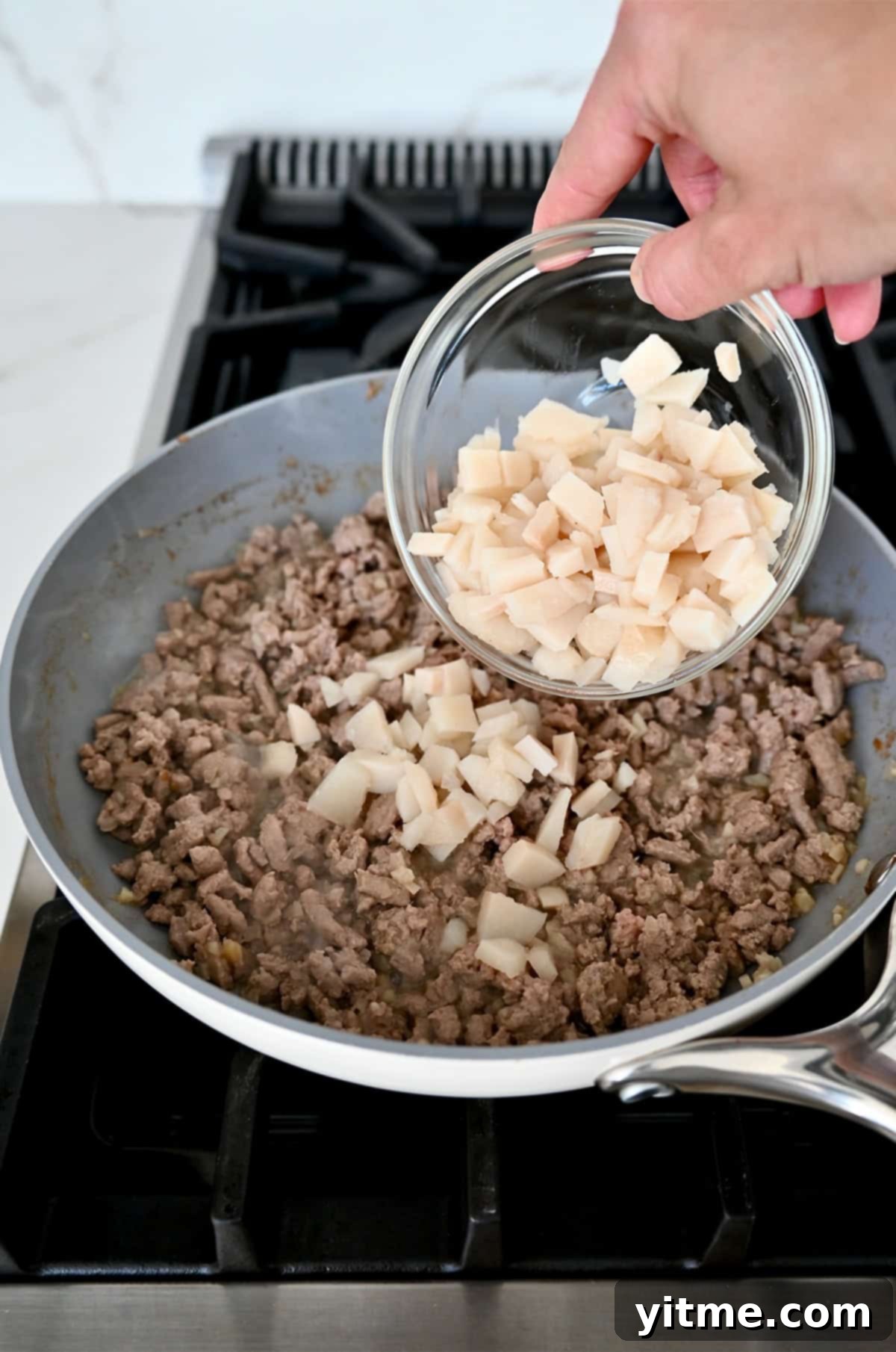Chopped water chestnuts being added to a skillet with browned meat.