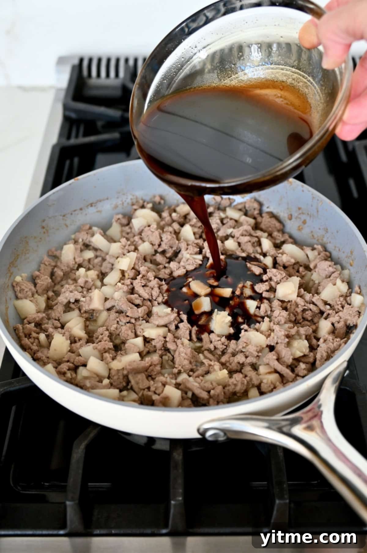 Savory sauce being added to cooked ground meat in a pan.