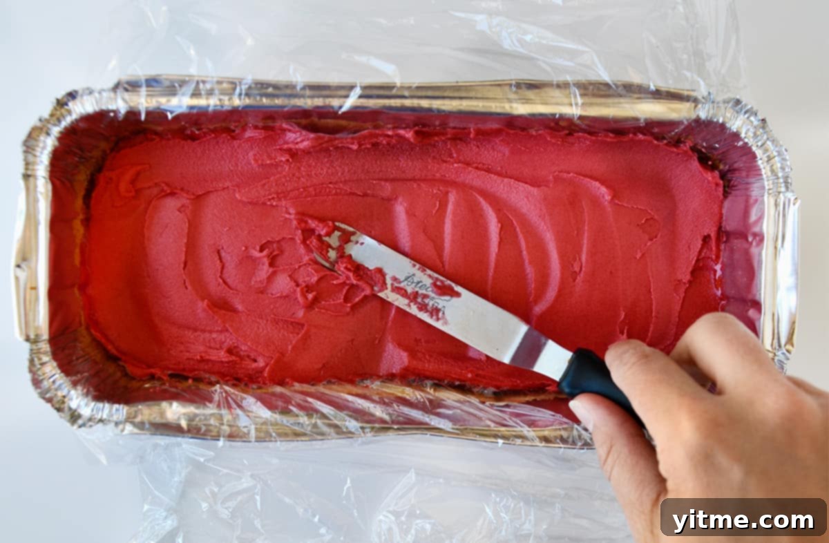 Spreading raspberry sorbet over pound cake in a plastic wrap-lined aluminum tray.