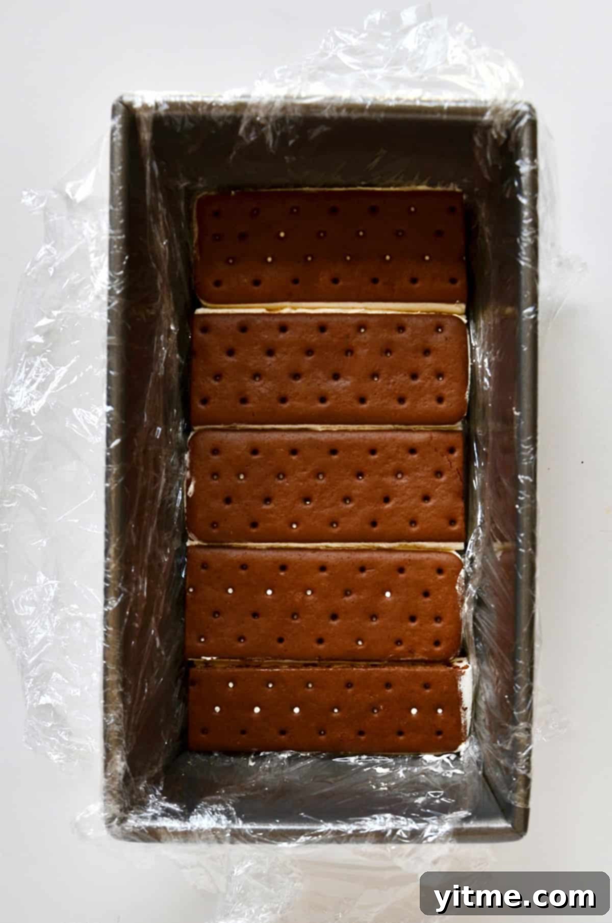 Ice cream sandwiches lining the bottom of a loaf pan lined with plastic wrap.