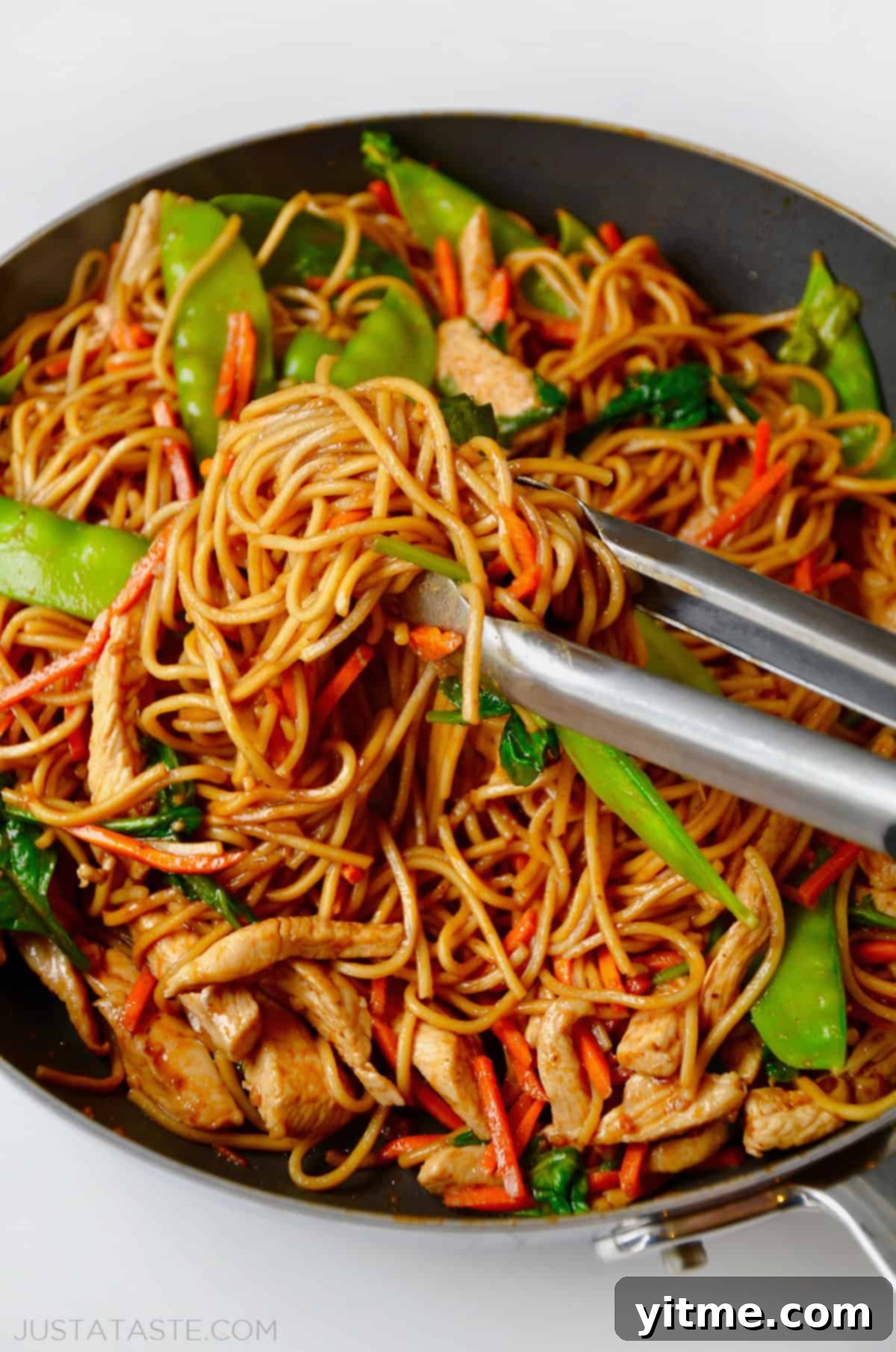 Chicken Lo Mein being served from a wok with tongs.