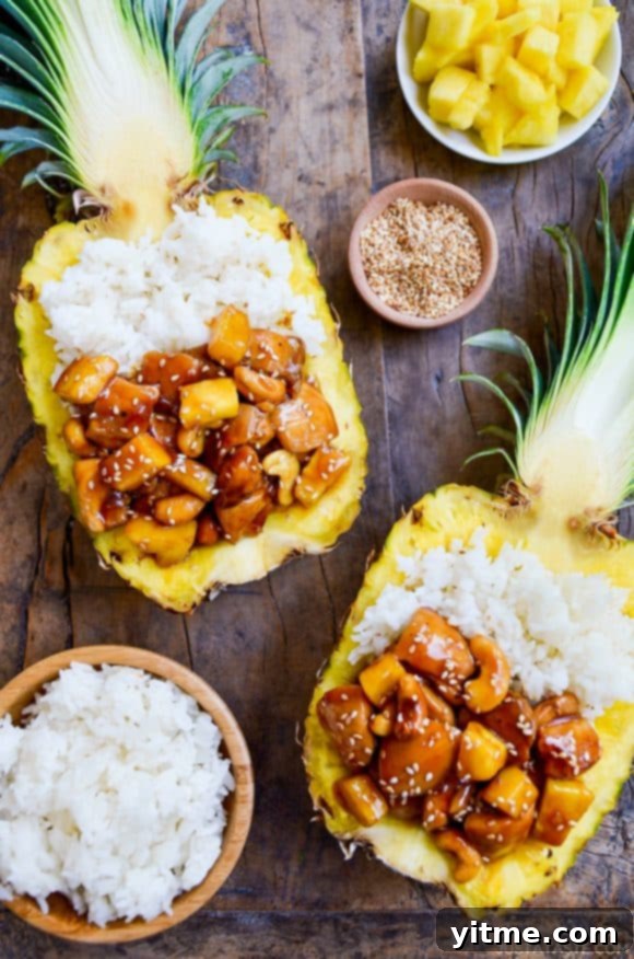 Two vibrant pineapple halves filled with golden sticky pineapple chicken and fluffy white rice, ready to serve
