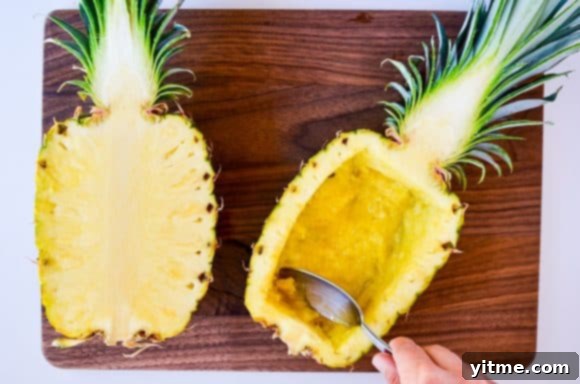 Fresh pineapples being carefully hollowed out with a spoon, showing the preparation for serving as bowls