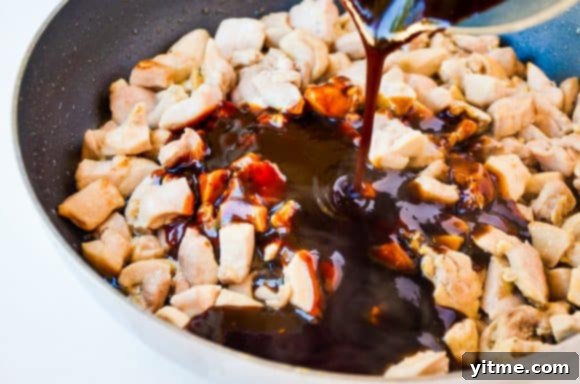 Diced chicken thighs with a rich, glossy pineapple sauce being drizzled over them in a skillet