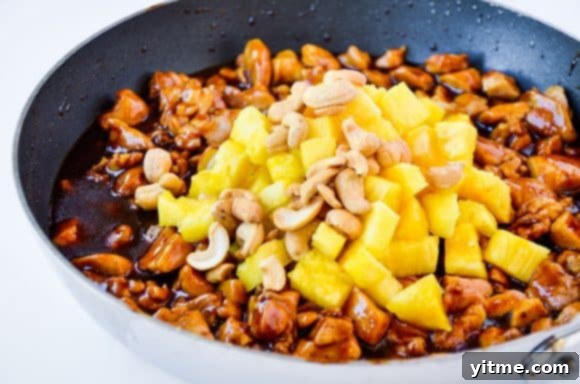 Sautéed chicken thighs topped with diced pineapple chunks and roasted cashews, illustrating the final dish components