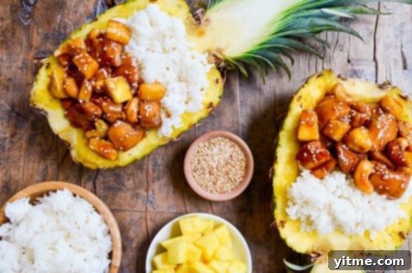 Multiple hollowed pineapples beautifully filled with Sticky Pineapple Chicken and white rice, garnished for presentation