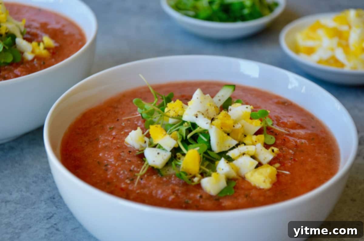 Bowl of gazpacho garnished with chopped egg and microgreens.